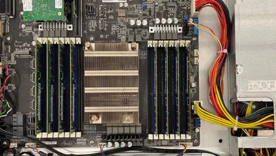 Draufsicht auf das Innere eines Servers mit zentralem Kühlkörper, umgeben von mehreren bestückten RAM-Steckplätzen und farbigen Stromkabeln auf der rechten Seite.